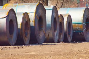 ENORMOUS COILS OF STEEL SHEETING SIT ON BARE EARTH